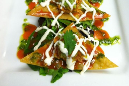 Two triangular nachos topped with meat, drizzled with sauce and garnished with cilantro, served on a bed of greens.