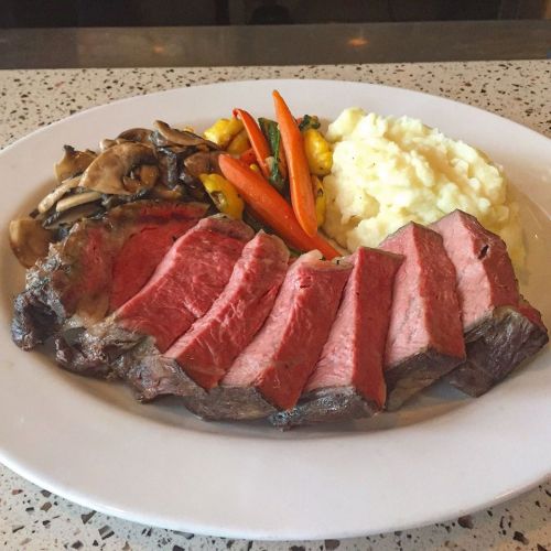 A plate of sliced beef steak with mashed potatoes and mixed vegetables, including carrots and mushrooms.