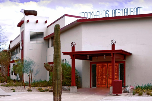 Exterior of Stockyards Restaurant featuring a cow statue on the roof and a cactus in front.