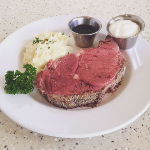 A plate featuring a slice of prime rib, mashed potatoes, and two small cups of sauce, garnished with parsley.