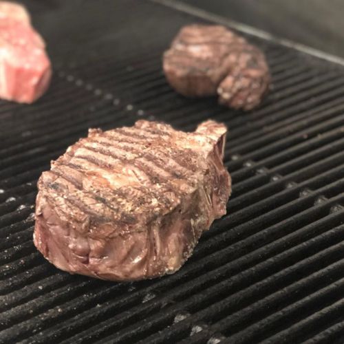 Grilled steaks with sear marks cooking on a barbecue grill.