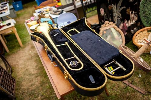 A trombone in a black case, surrounded by various items at a yard sale.