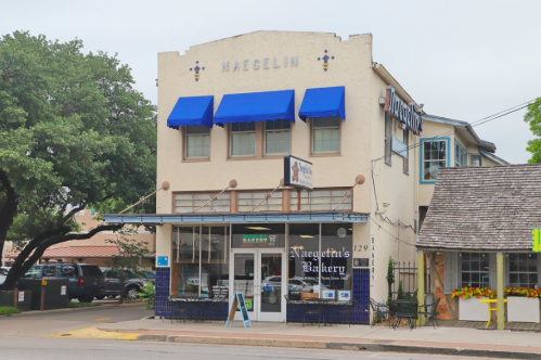 A charming bakery with blue awnings and a sign reading "Naegelin's Bakery," surrounded by trees and parked cars.