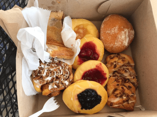 A box filled with assorted pastries, including donuts, fruit-filled danishes, and a flaky pastry.