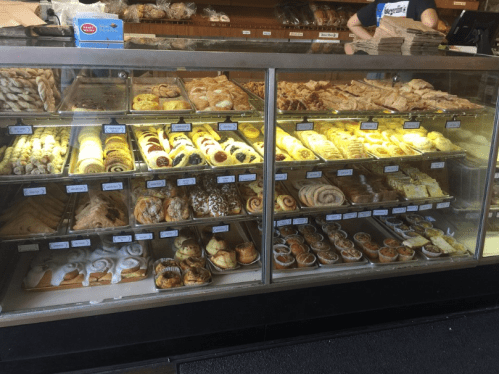 A display case filled with a variety of baked goods, including pastries, rolls, and desserts.
