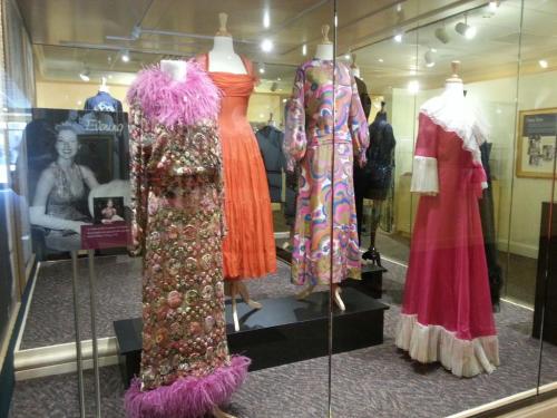 Display of vintage dresses in a glass case, featuring colorful patterns and unique designs from different eras.