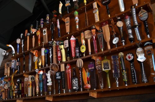 A wall display featuring a variety of colorful beer taps and handles in a bar setting.