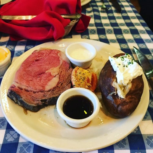 A plate featuring a slice of prime rib, a baked potato with sour cream, and a small dish of sauce.