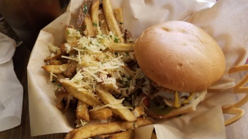 A burger with cheese and toppings beside a basket of golden fries topped with grated cheese and herbs.