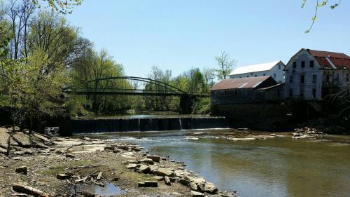 A serene river scene featuring a bridge, an old mill, and a small waterfall surrounded by trees and rocky banks.