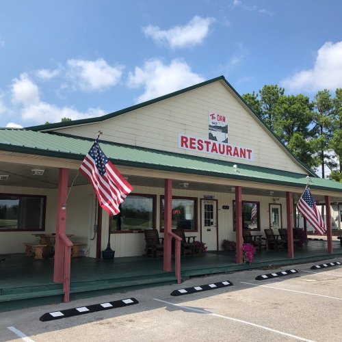 A restaurant building with a green roof, red accents, and American flags, set against a blue sky and trees.