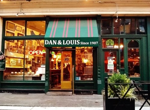 Exterior of Dan & Louis restaurant, featuring a green facade, striped awning, and an "OPEN" sign. Established in 1907.