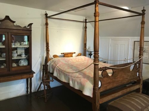 A vintage four-poster bed with a quilt, next to a wooden display cabinet filled with ceramics.