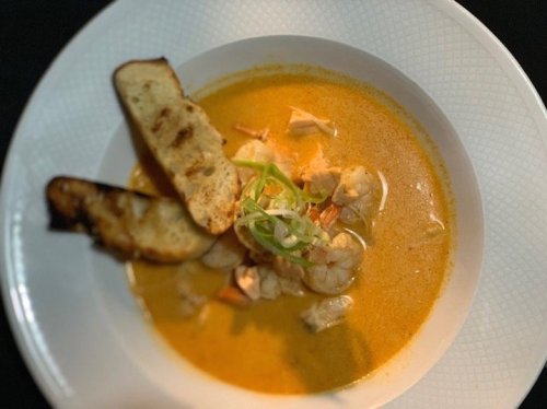A bowl of creamy shrimp soup garnished with green onions and served with toasted bread on the side.