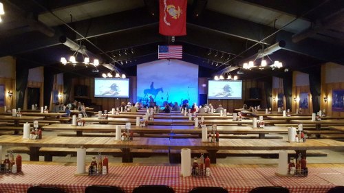 A spacious dining hall with wooden tables, an American flag, and screens displaying images, set for a gathering.