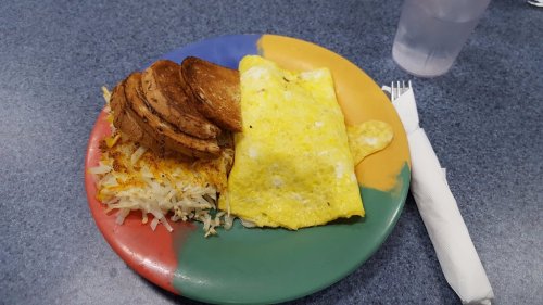 A colorful plate with a fluffy omelet, crispy hash browns, and golden-brown potato slices, alongside a glass of water.