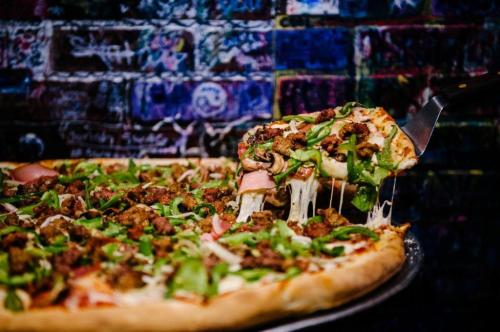 A close-up of a pizza topped with green peppers, mushrooms, and sausage, with a slice being lifted.