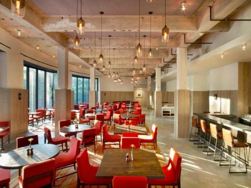 Modern restaurant interior with red chairs, wooden tables, and pendant lighting, featuring large windows and a spacious layout.