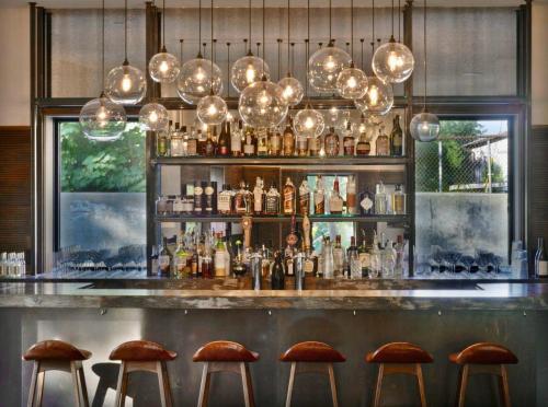 A stylish bar with a variety of bottles, illuminated by modern pendant lights, and wooden stools in front.