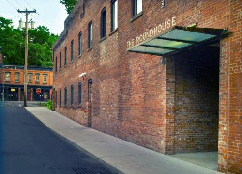 A brick building with a sign reading "The Roundhouse," located on a quiet street with trees in the background.
