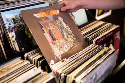 A person holds a vinyl record above a stack of various albums in a record store.