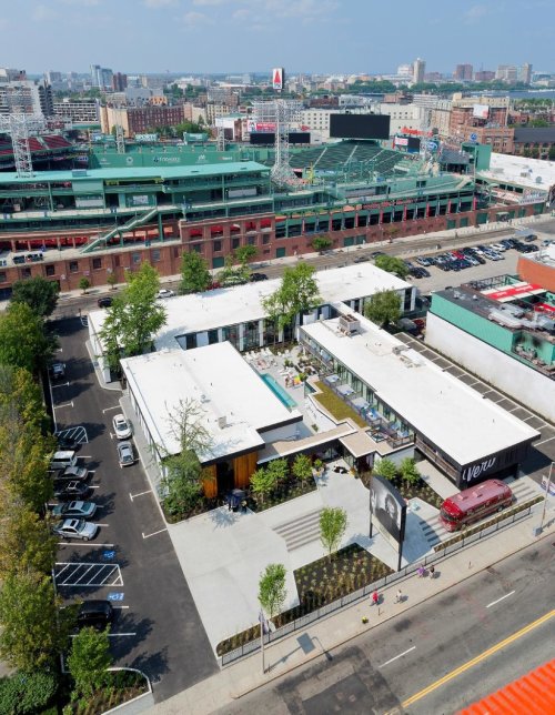 Aerial view of a modern building with a pool, surrounded by parking and cityscape, near a baseball stadium.