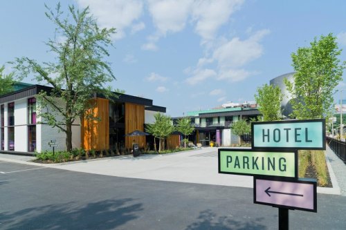 A modern hotel with colorful accents and a parking sign, surrounded by trees and a clear blue sky.