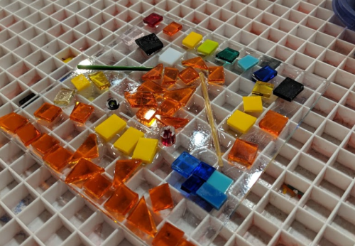 Colorful glass pieces arranged on a grid, featuring various shapes and sizes in orange, yellow, blue, and black.