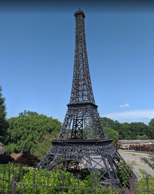 A miniature replica of the Eiffel Tower surrounded by trees and a clear blue sky.