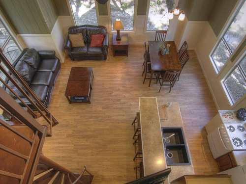 Aerial view of a cozy living space with a sofa, dining table, and kitchen area, featuring large windows and wooden floors.