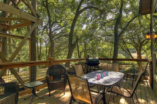 A wooden deck surrounded by trees, featuring a table with chairs and a grill, creating a cozy outdoor space.