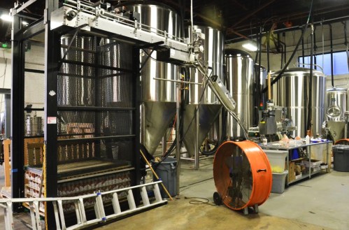 A brewery interior featuring large stainless steel tanks, a fan, and equipment for brewing processes.