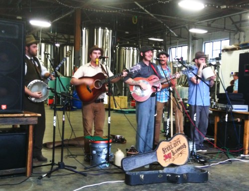 A band performs on stage in a brewery, playing various instruments like guitar, banjo, and drums.