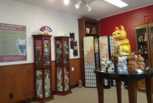 A room displaying various Maneki Neko figurines in glass cases, with a large golden cat statue on a table.