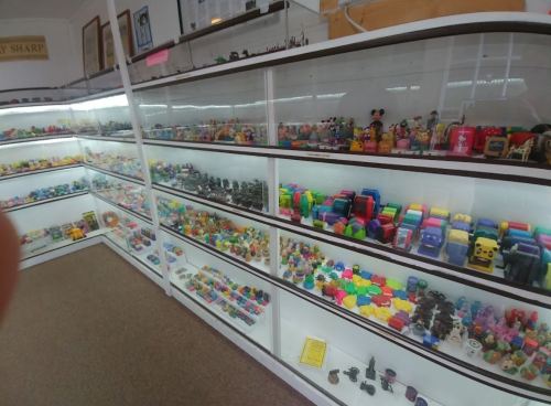 A display case filled with colorful toys and collectibles, including figures, cars, and various small items.