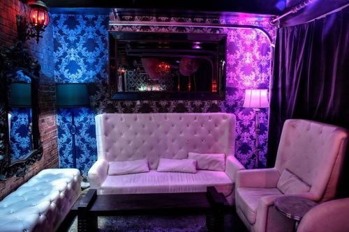 A stylish lounge with plush white furniture, colorful lighting, and ornate wallpaper, creating a cozy atmosphere.
