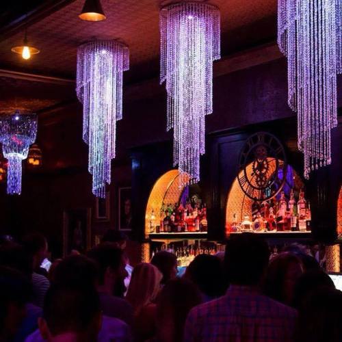 A vibrant bar scene with colorful chandeliers and a crowd enjoying the atmosphere.