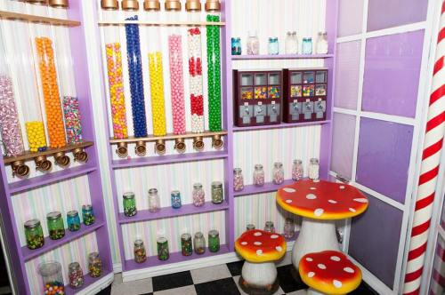 Colorful candy dispensers and jars filled with sweets, featuring whimsical mushroom-shaped stools in a vibrant candy shop.