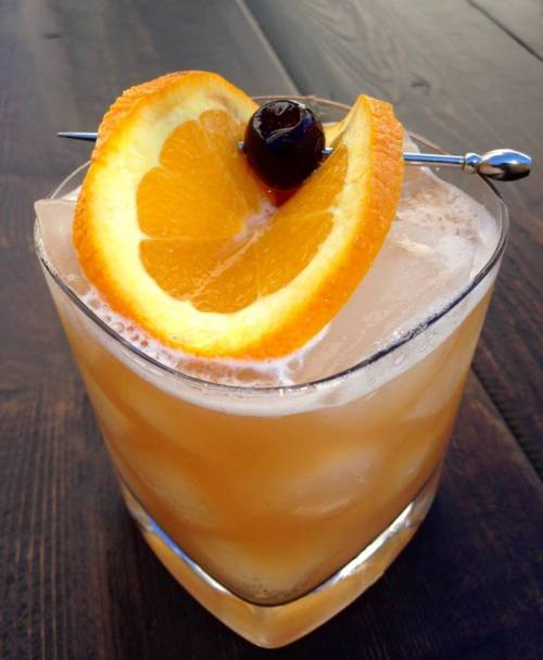 A refreshing cocktail in a glass, garnished with an orange slice and a cherry, served over ice.