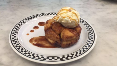 A warm cinnamon roll topped with vanilla ice cream and drizzled with caramel sauce on a checkered plate.