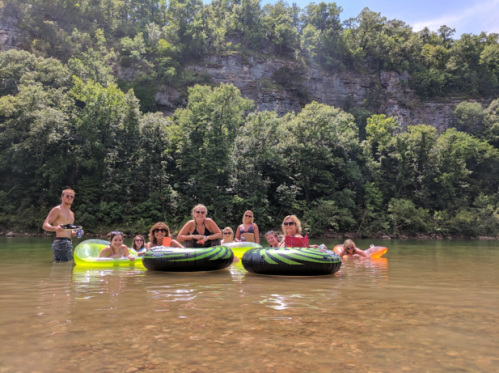 A group of people enjoying a summer day in a river, floating on inflatable tubes surrounded by lush greenery.