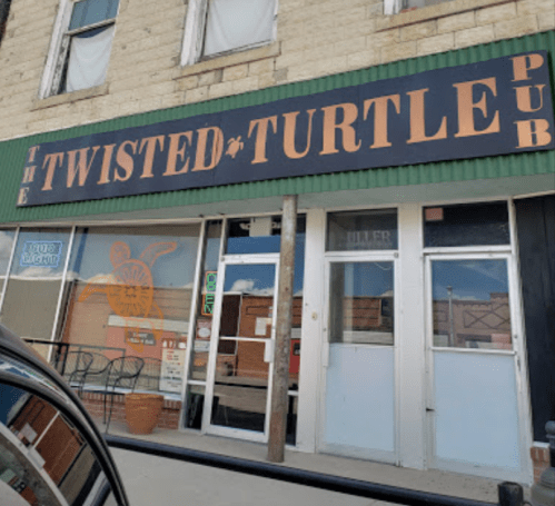 Exterior of The Twisted Turtle Pub, featuring a green awning and large sign, with outdoor seating visible.