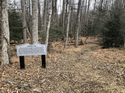 A forest path with a sign about the Pisgah Fire, surrounded by trees and dry leaves.