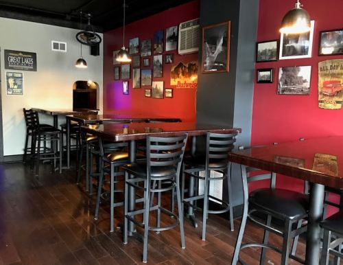 A cozy bar interior with wooden tables, high chairs, and red walls adorned with framed photos.