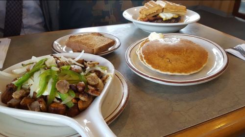 A table with three plates: a vegetable and sausage stir-fry, a pancake with butter, and a waffle sandwich.