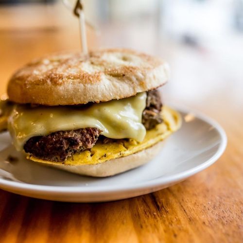 A close-up of a delicious burger with melted cheese on a toasted bun, served on a white plate.
