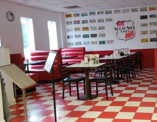 Interior of a diner featuring red booths, checkered floor, and a wall adorned with vintage license plates.