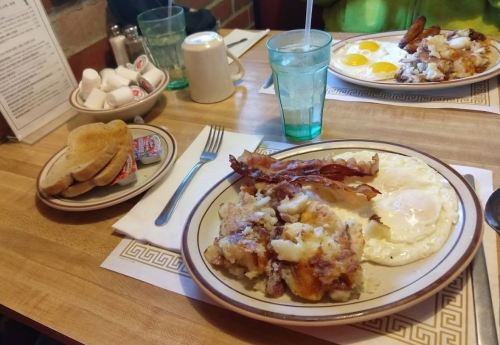 A breakfast plate with eggs, bacon, and hash browns, alongside toast and a glass of water on a wooden table.