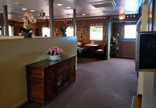 Interior of a restaurant featuring a wooden cabinet, floral decorations, and cozy seating areas.