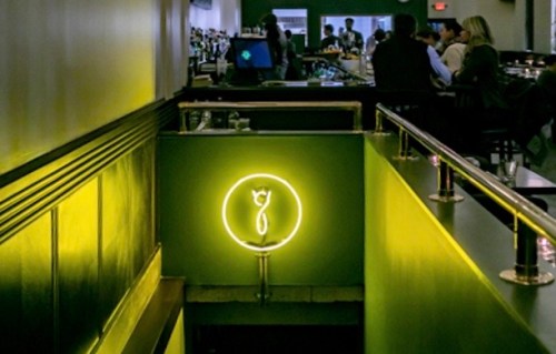 A dimly lit bar entrance with a glowing green neon sign and patrons in the background.